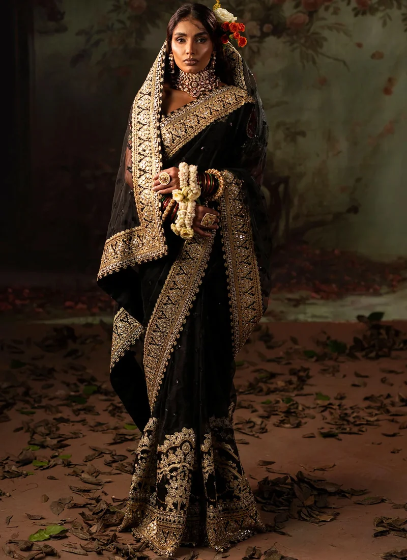 Black Reception Saree with Gold Panni Border Black bridal saree, seated three-quarter view, showing gold floral embroidery around the hem.
