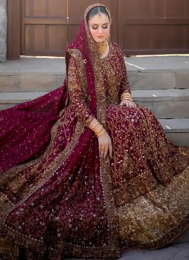Burgundy bridal gown seated view with flowing dupatta and shimmering bronze-gold farshi lehenga