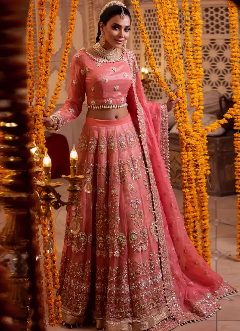 Coral Walima Lehenga Choli with Pearl-Drop Choli Hem Coral pink bridal lehenga choli in three-quarter front view with gold floral embroidery and a wide ornate hem.