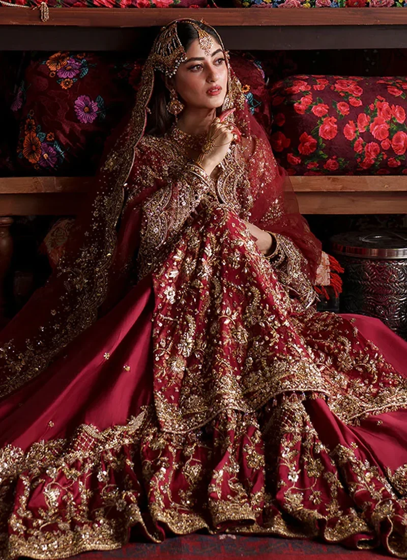 Deep red farshi lehenga seated view showing gold floral embroidery and a sweeping layered hem