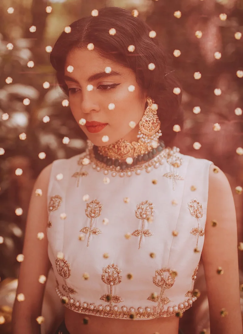 Emerald green lehenga seated full-length view with gold floral hem and pink embroidered dupatta