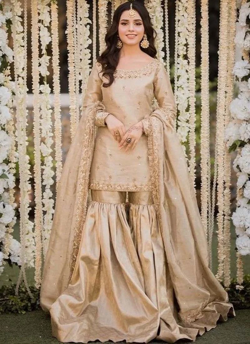 Gold Nikkah Gharara Suit with Kiran-Lace Dupatta Border Gold gharara suit angled side view with fitted sleeves, embroidered cuffs and gathered trousers