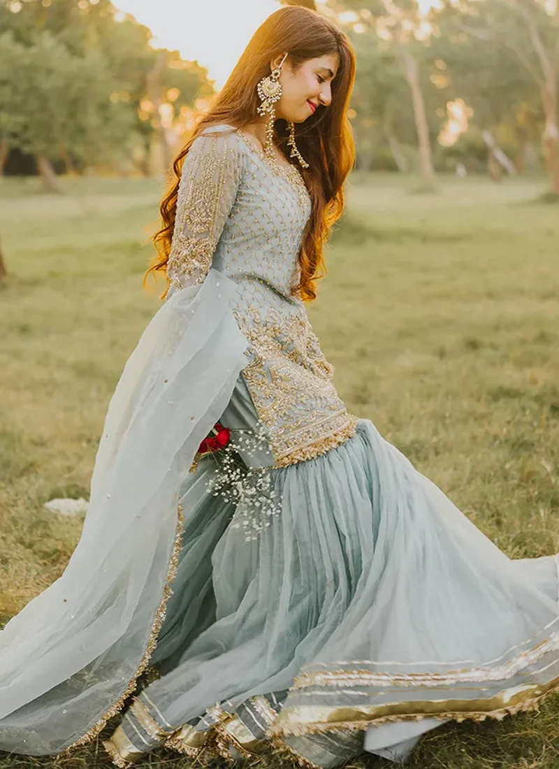 Ice blue gharara suit walking view with a gold embroidered shirt and softly gathered flared bottoms