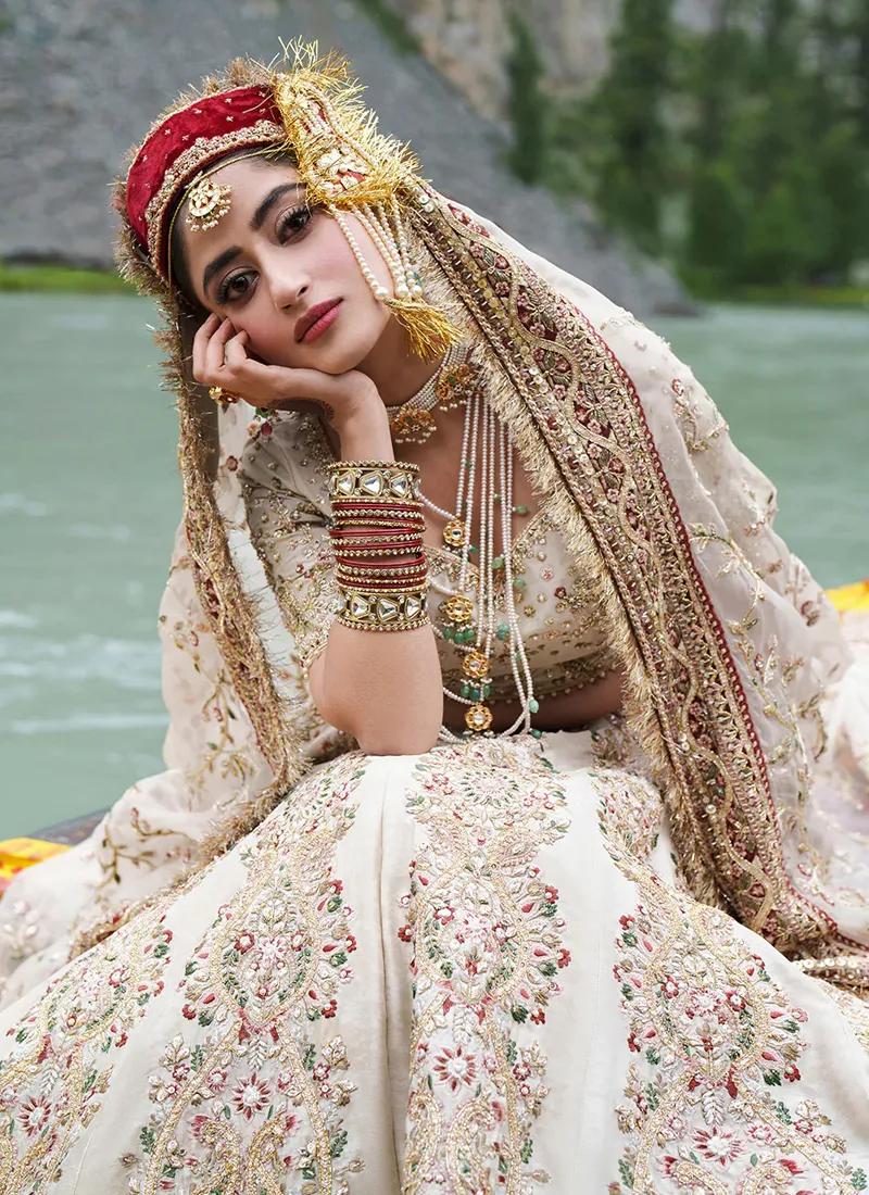 Close seated view of floral-paisley lehenga embroidery with pink blossoms and green leaves beside the maroon-backed dupatta border and kiran fringe