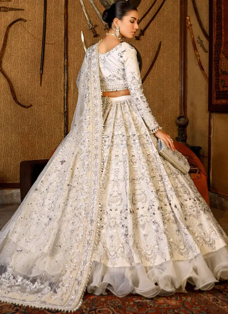 Ivory lehenga choli side view showing silver embroidered skirt panels and a rippling organza ruffle hem.