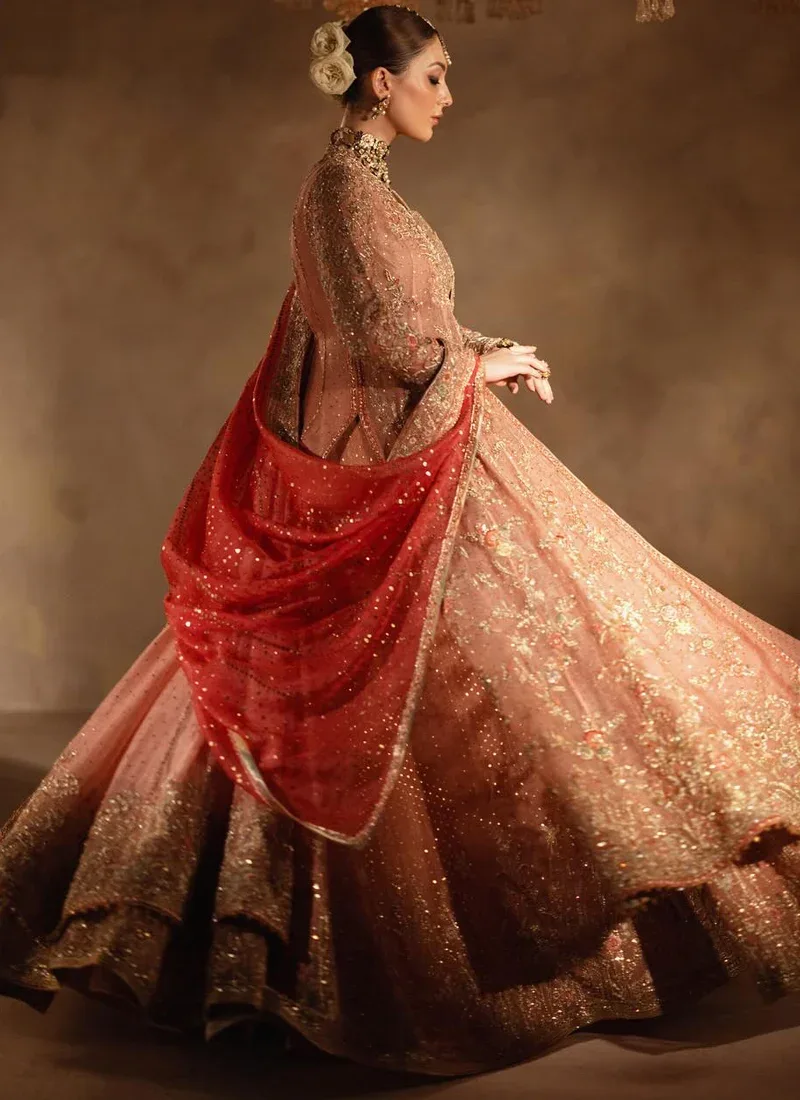 Dusty peach bridal gown and lehenga in side motion with a sweeping embroidered hem and coral dupatta.
