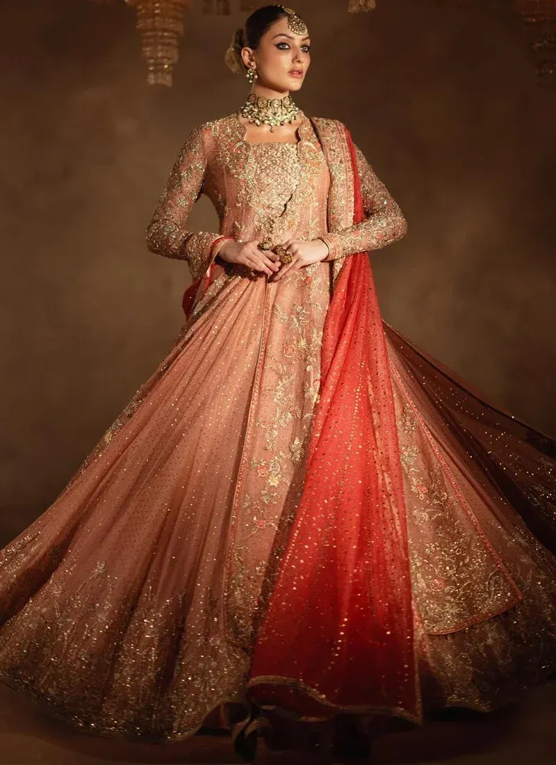 Dusty peach bridal gown and flared lehenga in a turning view, showing ornate gold hem embroidery.