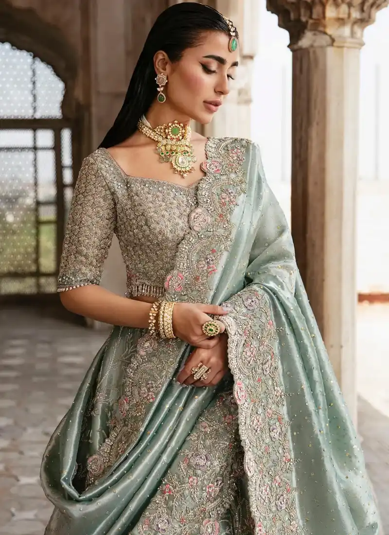 Sage green lehenga choli close-up showing dense blouse embroidery and a scalloped floral dupatta border.