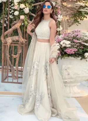 White lehenga choli, seated front view with silver floral motifs and a diamond-lattice sleeveless blouse.