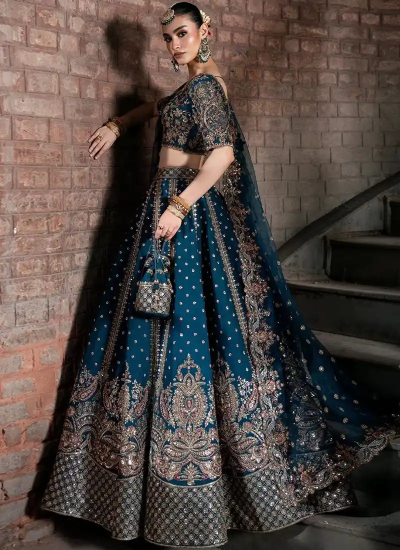 Zinc blue walima lehenga choli seated side view with sweeping paisley hem and scalloped dupatta border